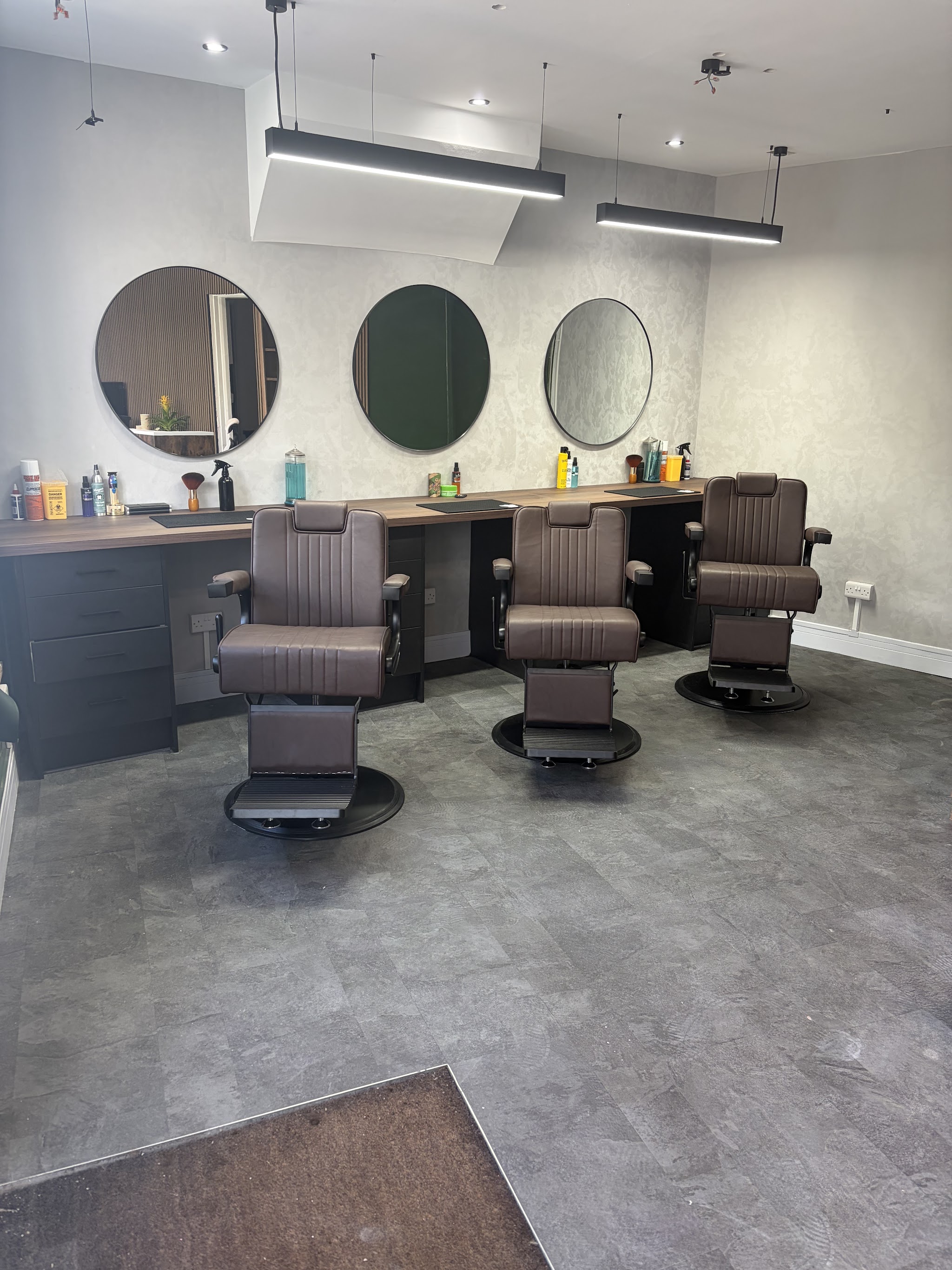 Three brown barber chairs with round mirrors and timber worktops